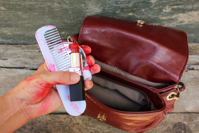 A hand pulls out melted lipstick and a messy comb and mirror from a purse.