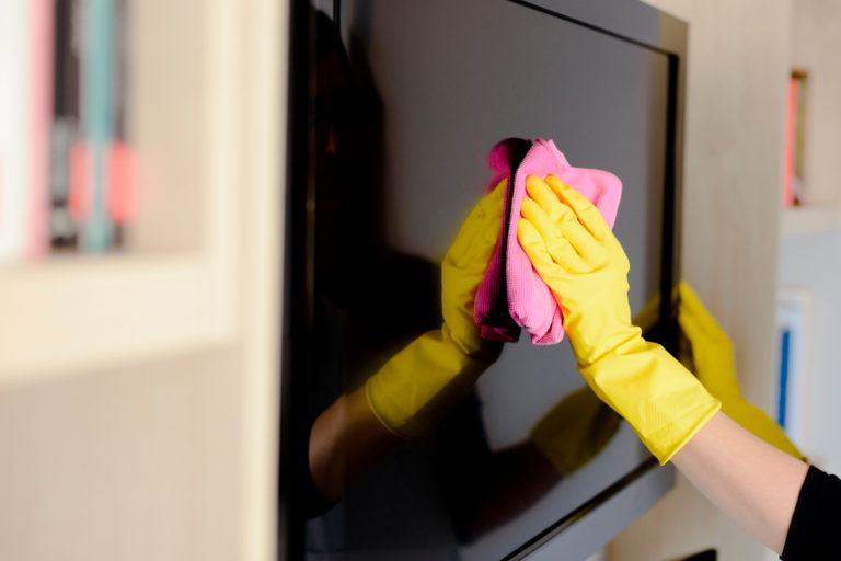 A person wearing gloves wiping down a flat screen tv.