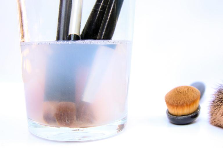 Makeup brushes soaking in a glass filled with water and vinegar.