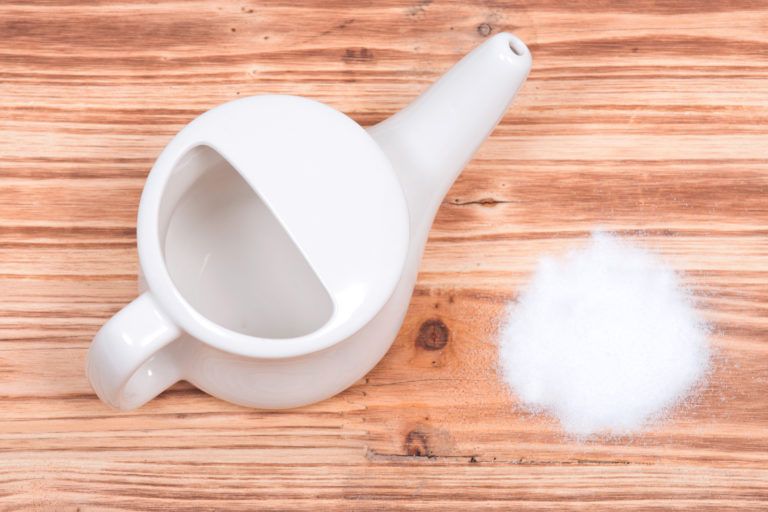 A neti pot with table salt sitting next to it.