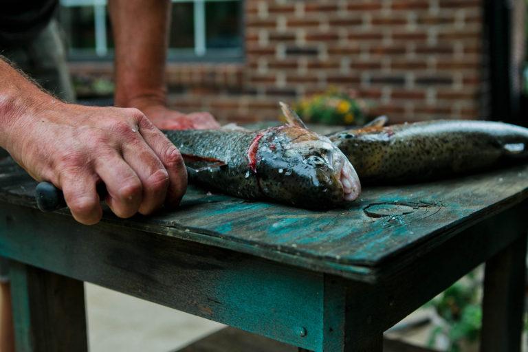 A man cleaning a trout outside.