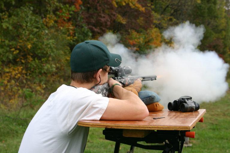 A young man shooting a muzzleloader rifle.