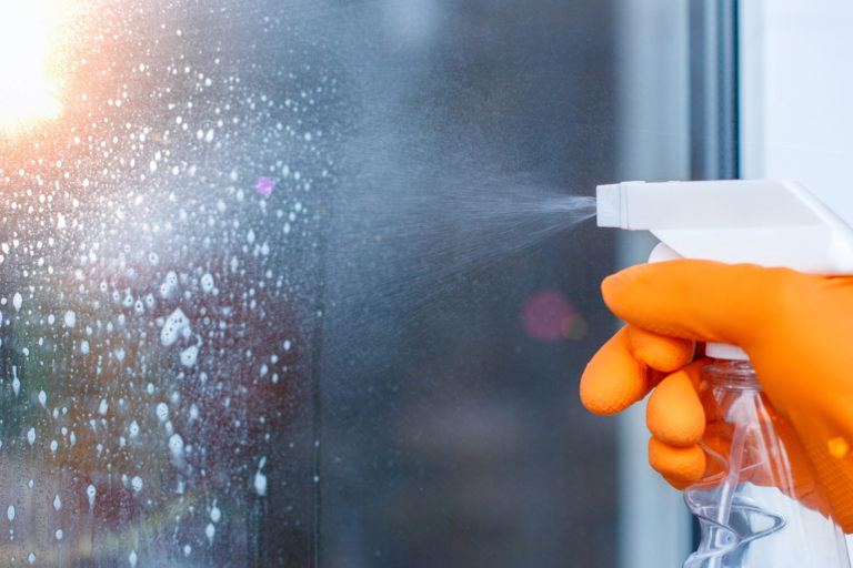 A gloved hand cleans a glass window.